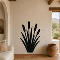 Black metal cattail wall art silhouette with multiple reed stems and seed heads, mounted on a beige living room wall above a sofa.