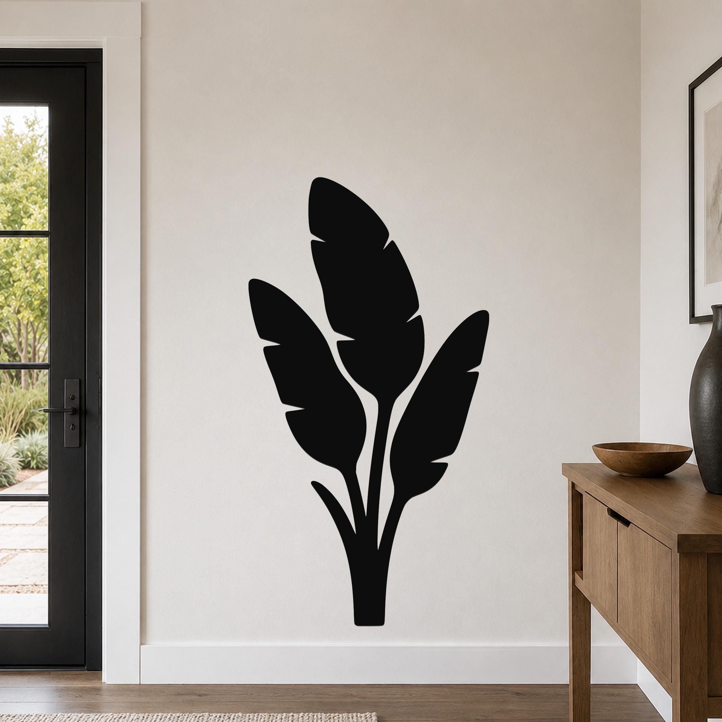 Black metal wall art featuring a tropical leaf silhouette, mounted on a living room wall above a wooden console table.