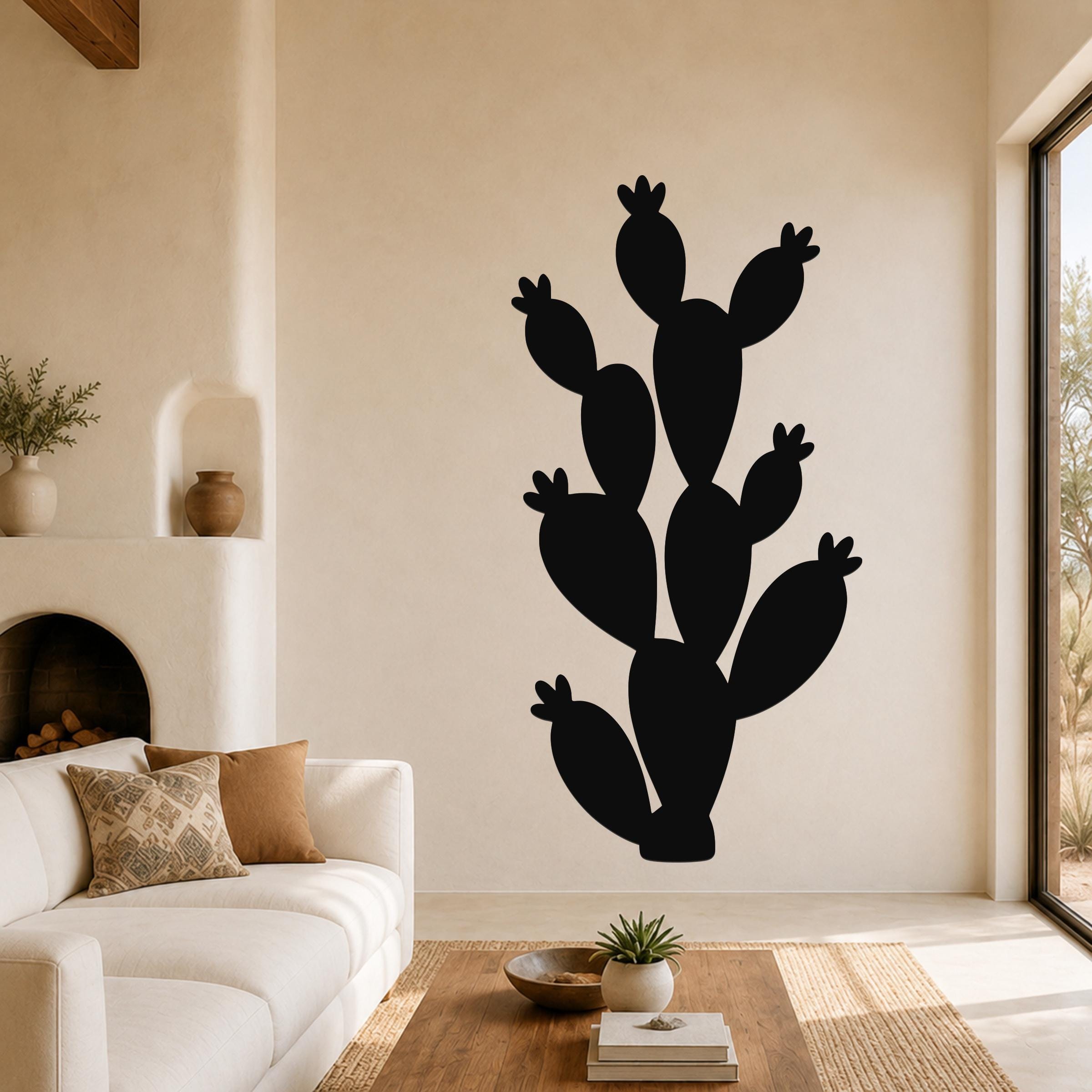 Black metal prickly pear cactus wall art with multiple segmented arms and flower cutouts, mounted on a living room wall above a white sofa.