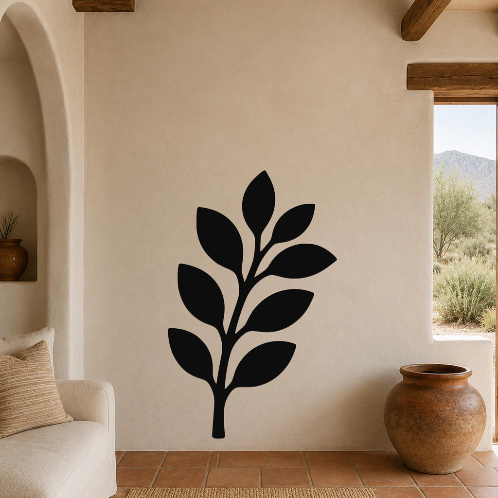 Black metal olive branch wall art with leaf cutouts, mounted on a beige stucco wall in a living room with terracotta flooring and wooden beams.