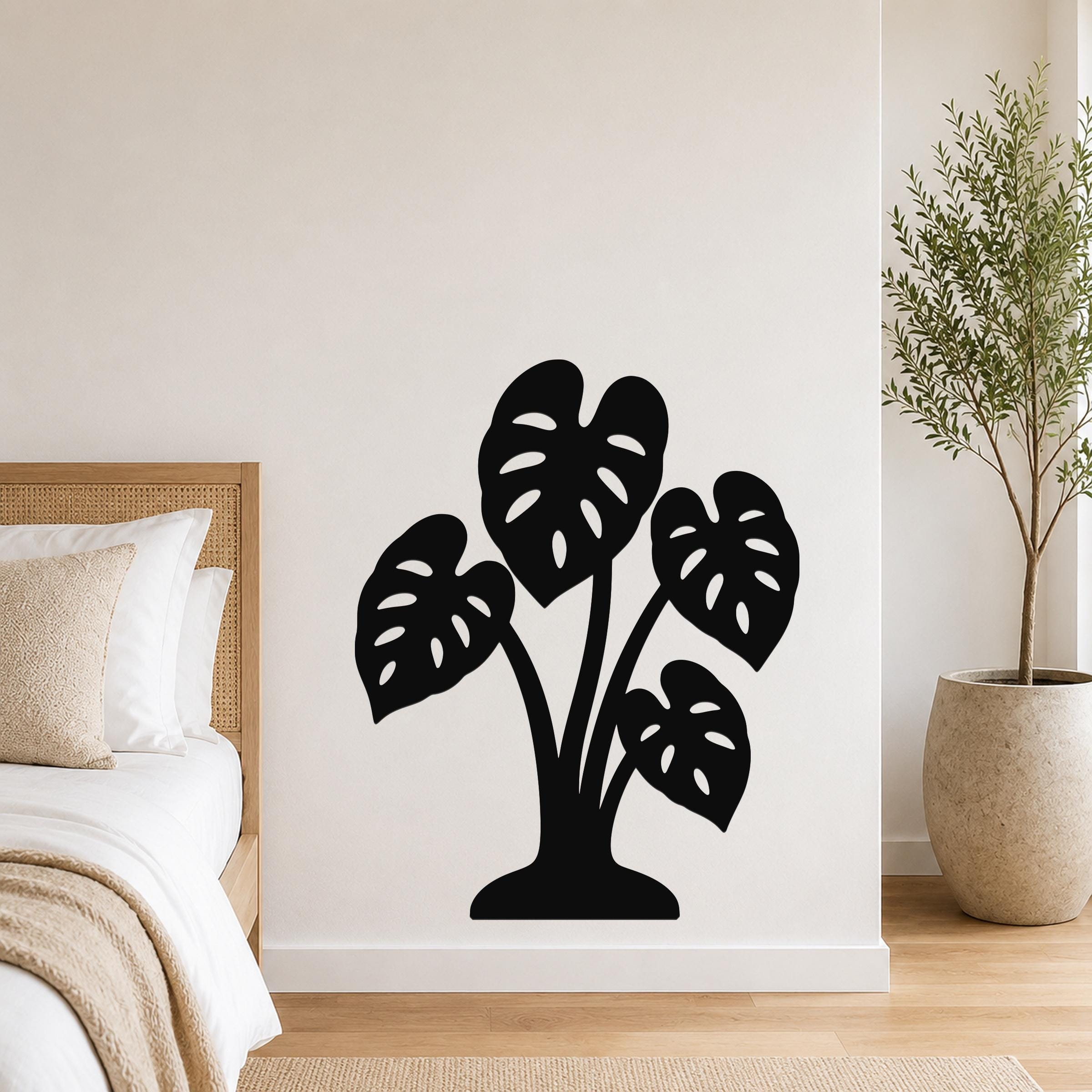 Black metal wall art cutout of a monstera plant with leaf perforations, mounted on a bedroom wall above a bed.