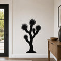 Black metal Joshua tree wall art with starburst-shaped branches, mounted on a white wall in a modern entryway.