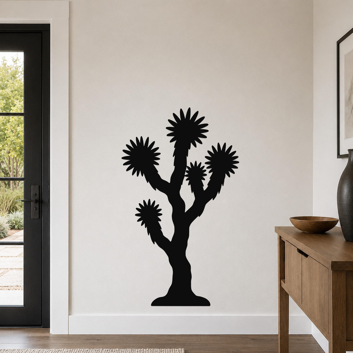 Black metal Joshua tree wall art with starburst-shaped branches, mounted on a white wall in a modern entryway.