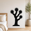 Black metal Joshua tree wall art with starburst-shaped branches, mounted on a white bedroom wall above a bed.