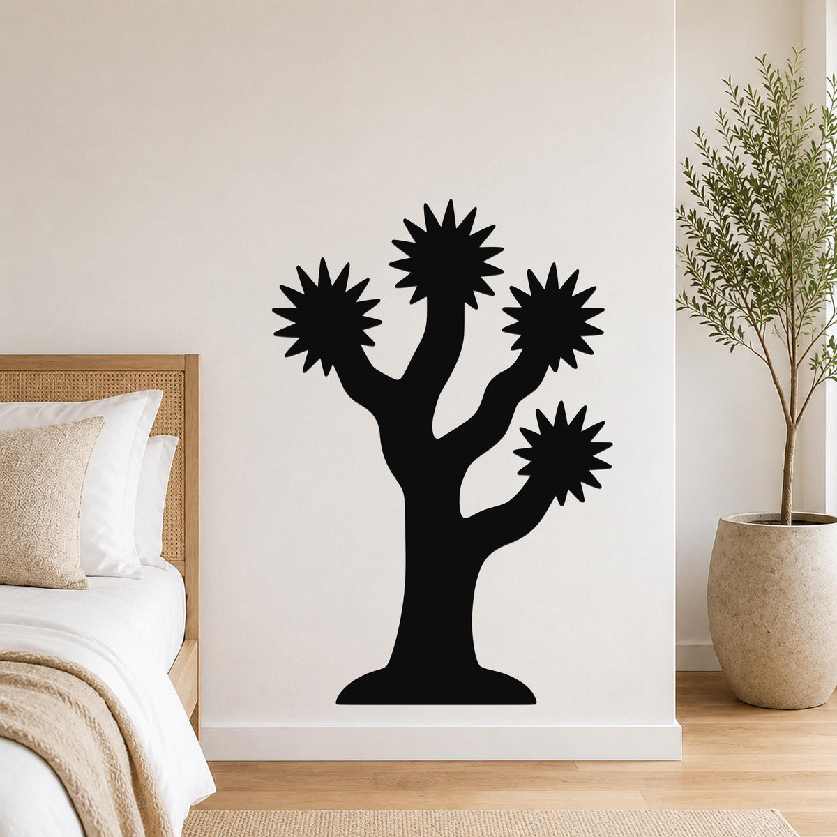 Black metal Joshua tree wall art with starburst-shaped branches, mounted on a white bedroom wall above a bed.