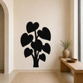 Black metal wall art in the silhouette of a plant with heart-shaped leaves, mounted on a beige wall above a wooden bench in a minimalist entryway.