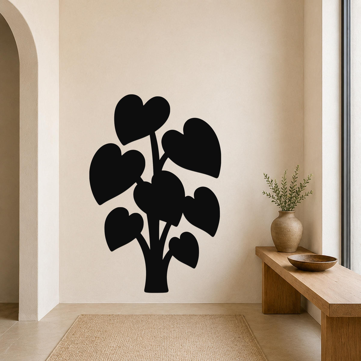 Black metal wall art in the silhouette of a plant with heart-shaped leaves, mounted on a beige wall above a wooden bench in a minimalist entryway.