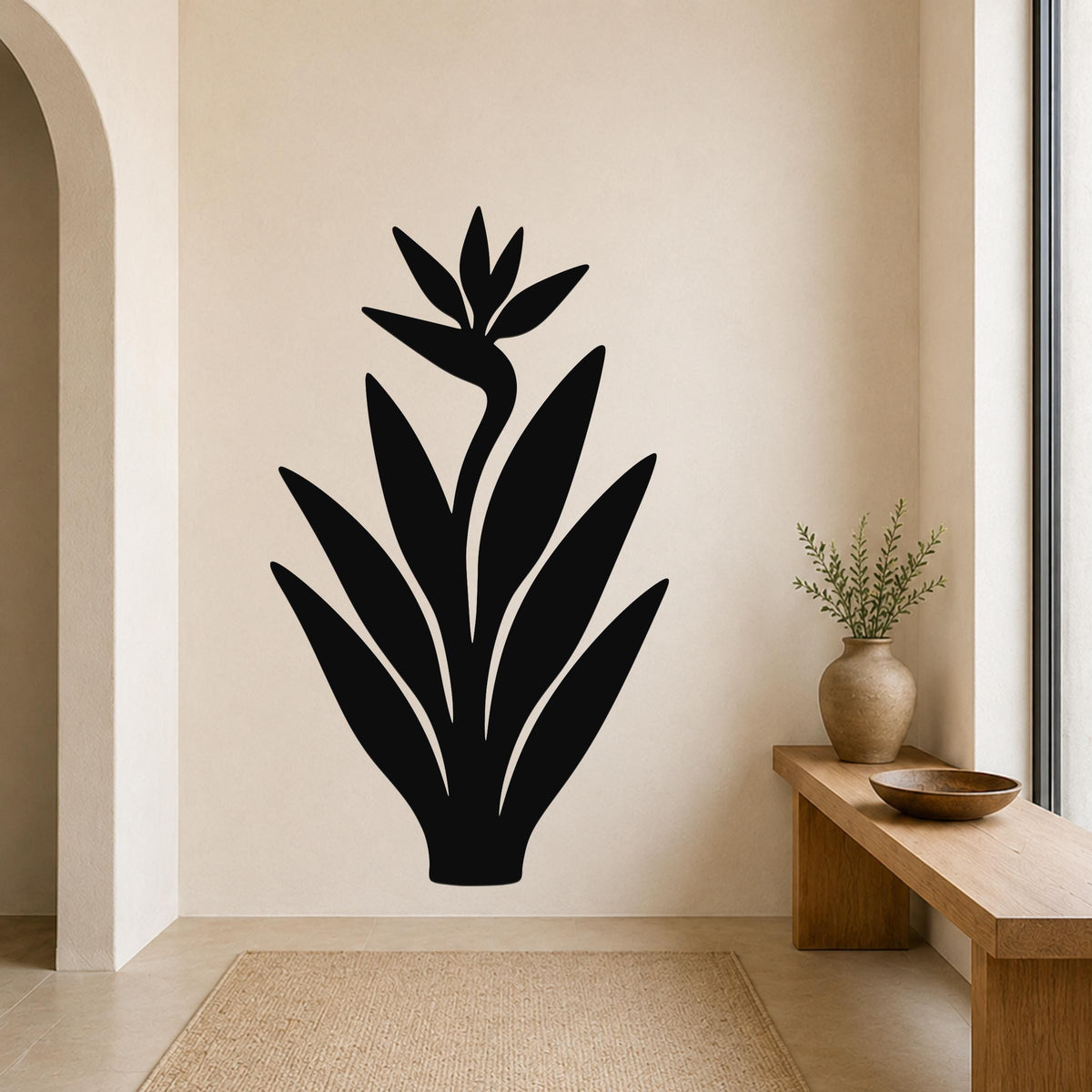 Black metal Bird of Paradise wall art with a silhouette design, mounted on a beige wall above a wooden bench in a minimalist entryway.