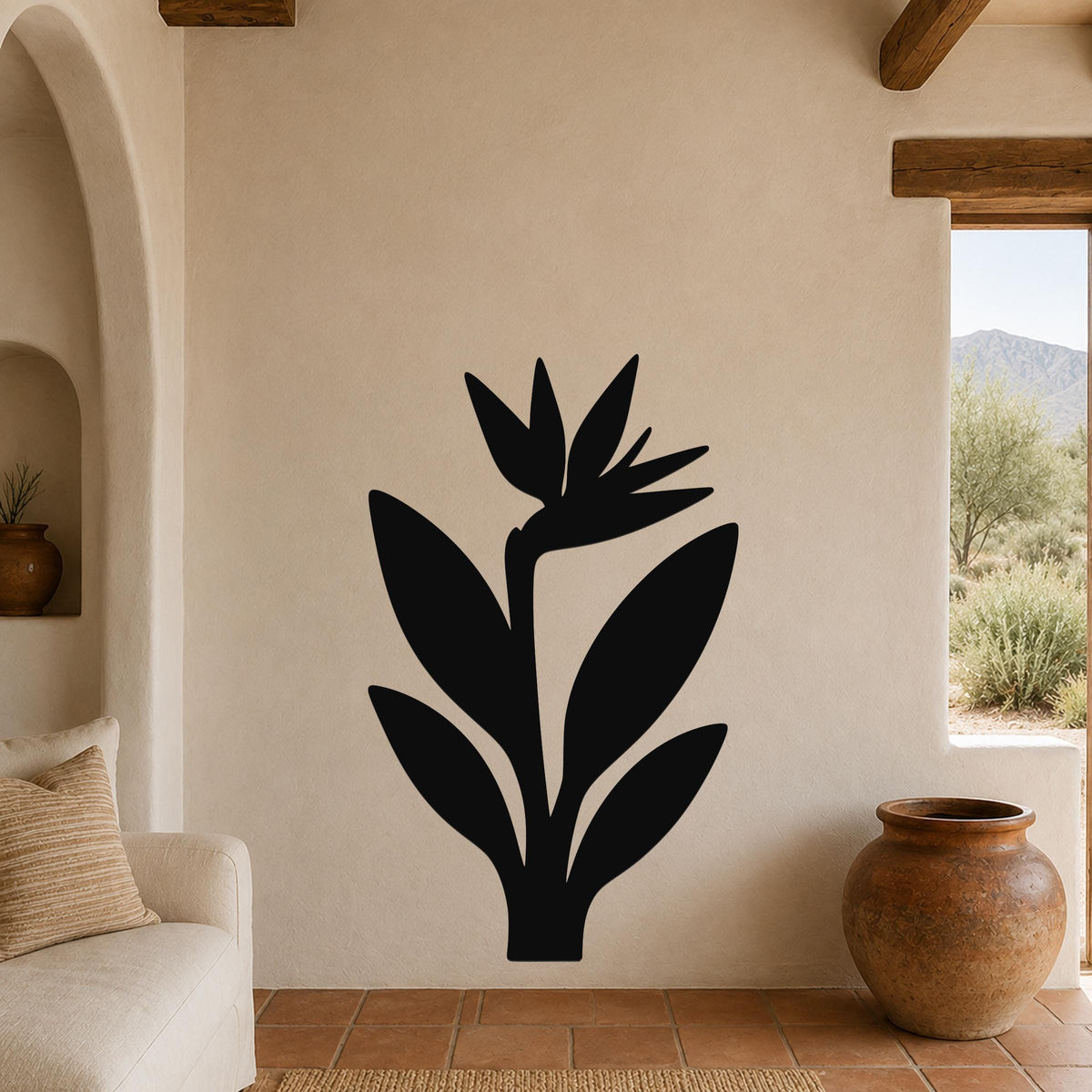 Black metal Bird of Paradise wall art silhouette mounted on a beige living room wall above a sofa, with a terracotta vase and arched doorway visible nearby.