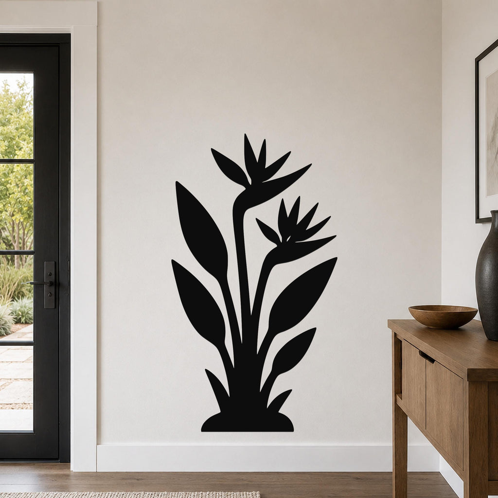 Black metal wall art silhouette of a bird of paradise plant with two flowers and long leaves, mounted on a living room wall above a wooden console table.