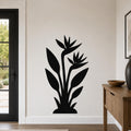 Black metal wall art silhouette of a bird of paradise plant with two flowers and long leaves, mounted on a living room wall above a wooden console table.