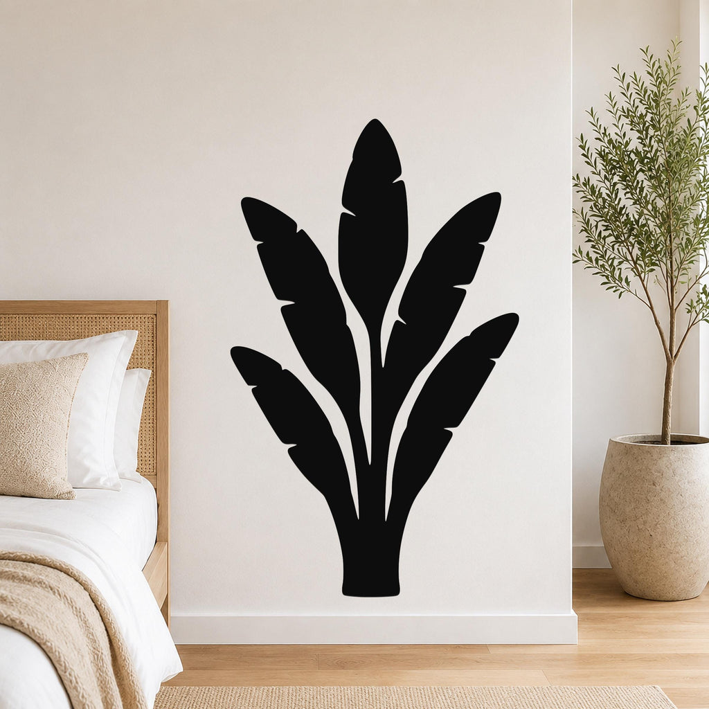 Black metal wall art in a banana plant silhouette with leaf cutouts, mounted on a bedroom wall above a bed.