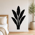 Black metal wall art in a banana plant silhouette with leaf cutouts, mounted on a bedroom wall above a bed.