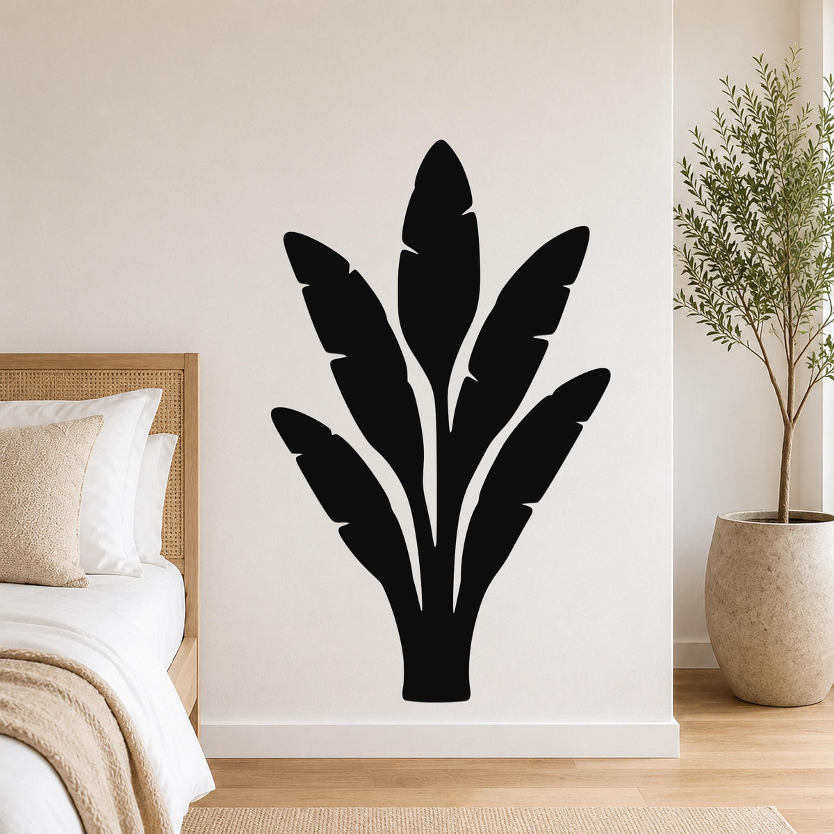 Black metal wall art in a banana plant silhouette with leaf cutouts, mounted on a bedroom wall above a bed.