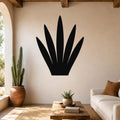 Black metal wall art in the silhouette of a century plant, mounted on a beige living room wall above a wooden coffee table.