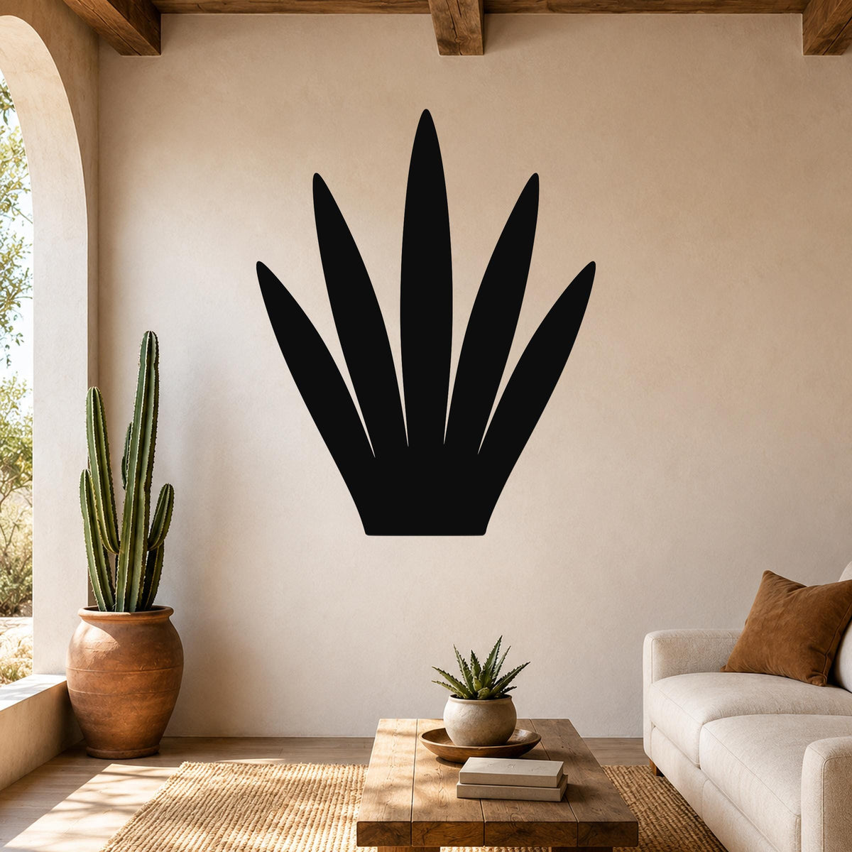 Black metal wall art in the silhouette of a century plant, mounted on a beige living room wall above a wooden coffee table.