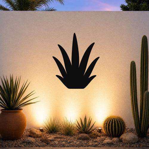Black metal agave wall art silhouette mounted on a white outdoor wall above a desert garden with cacti and warm uplighting.