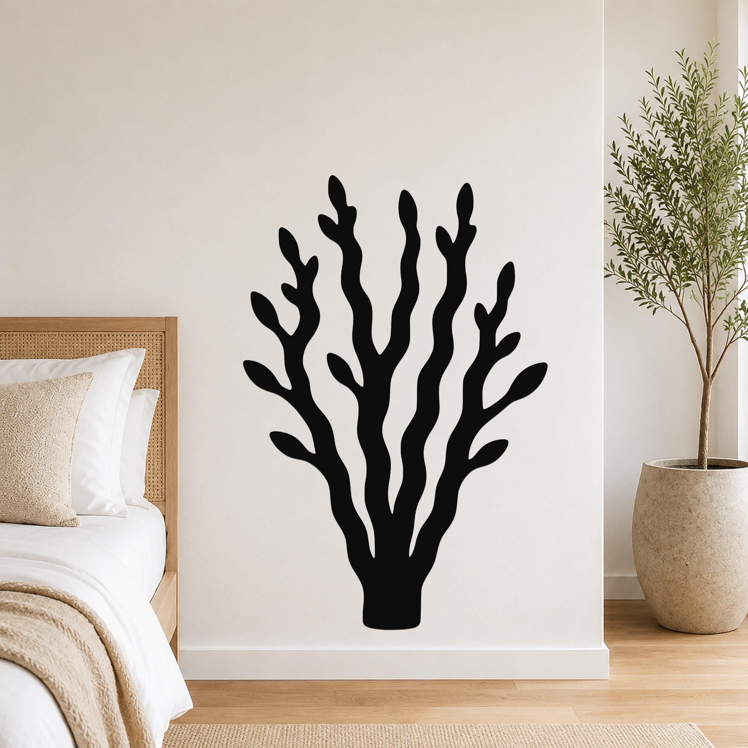 Black metal wall art in a kelp or seaweed silhouette design, mounted on a white bedroom wall above a bed with a woven headboard.