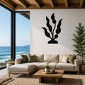 Black metal kelp wall art with flowing leaf cutouts, mounted on a white living room wall above a beige sectional sofa.