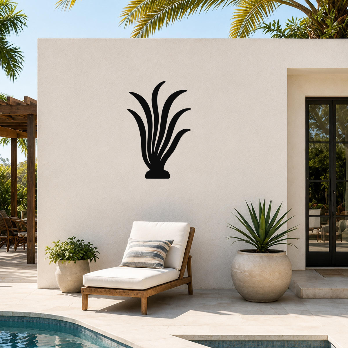 Black metal kelp wall art with flowing leaf cutouts, mounted on a white outdoor wall beside a poolside lounge chair.