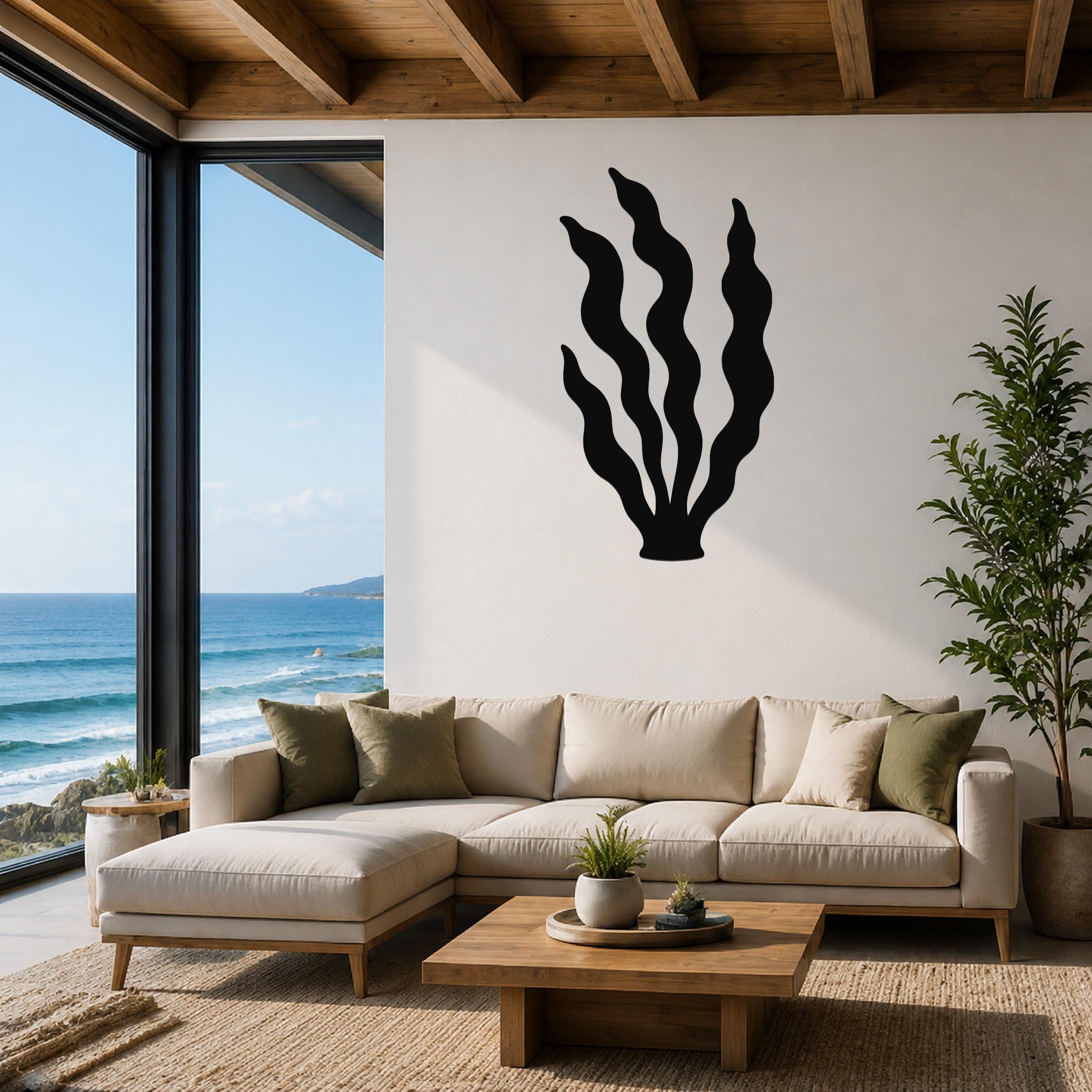 Black metal kelp wall art with wavy blade cutouts, mounted above a beige sectional sofa in a coastal living room with ocean views.