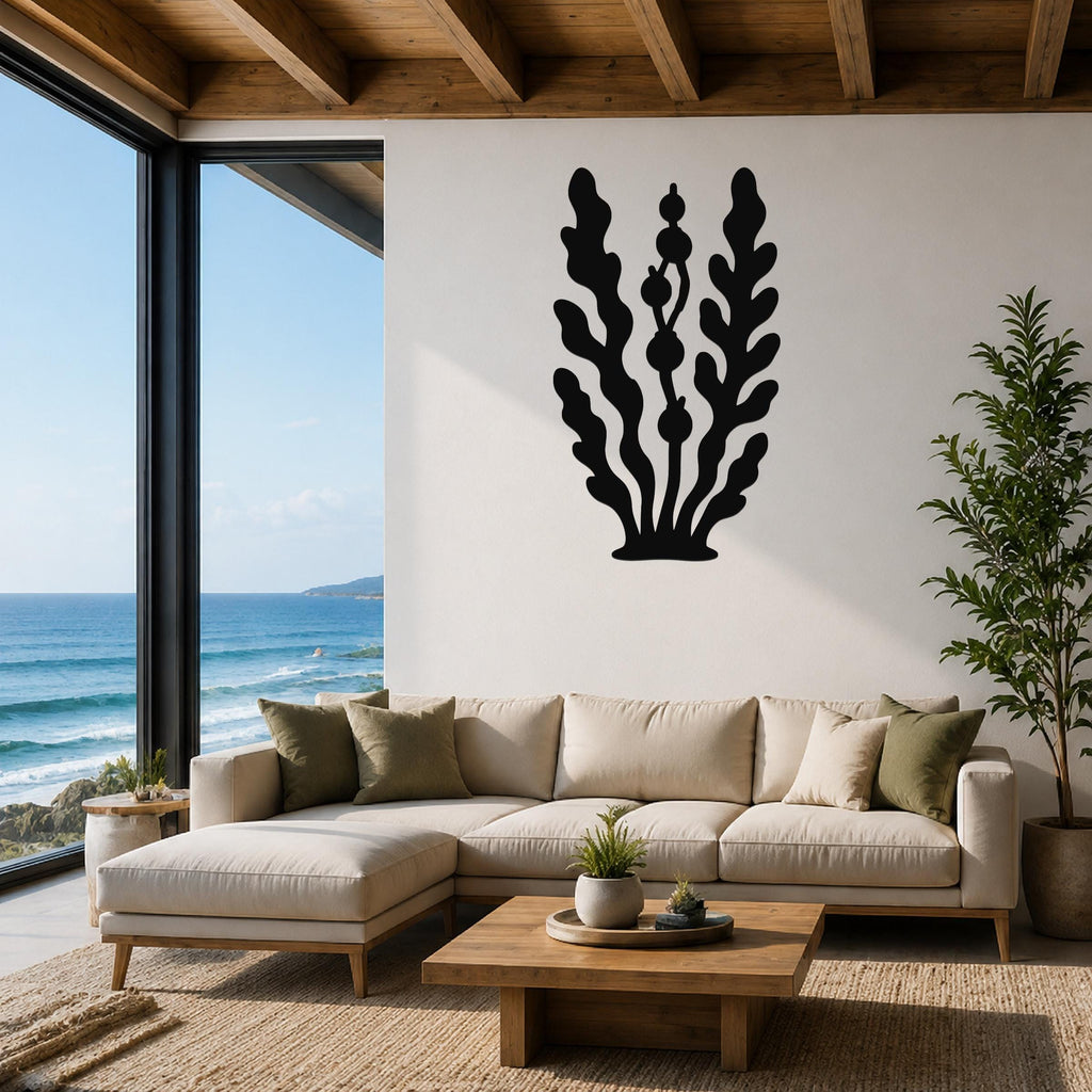 Black metal kelp and seaweed wall art with leafy fronds and bulbous cutouts, mounted on a white wall above a beige sectional sofa in a coastal living room.