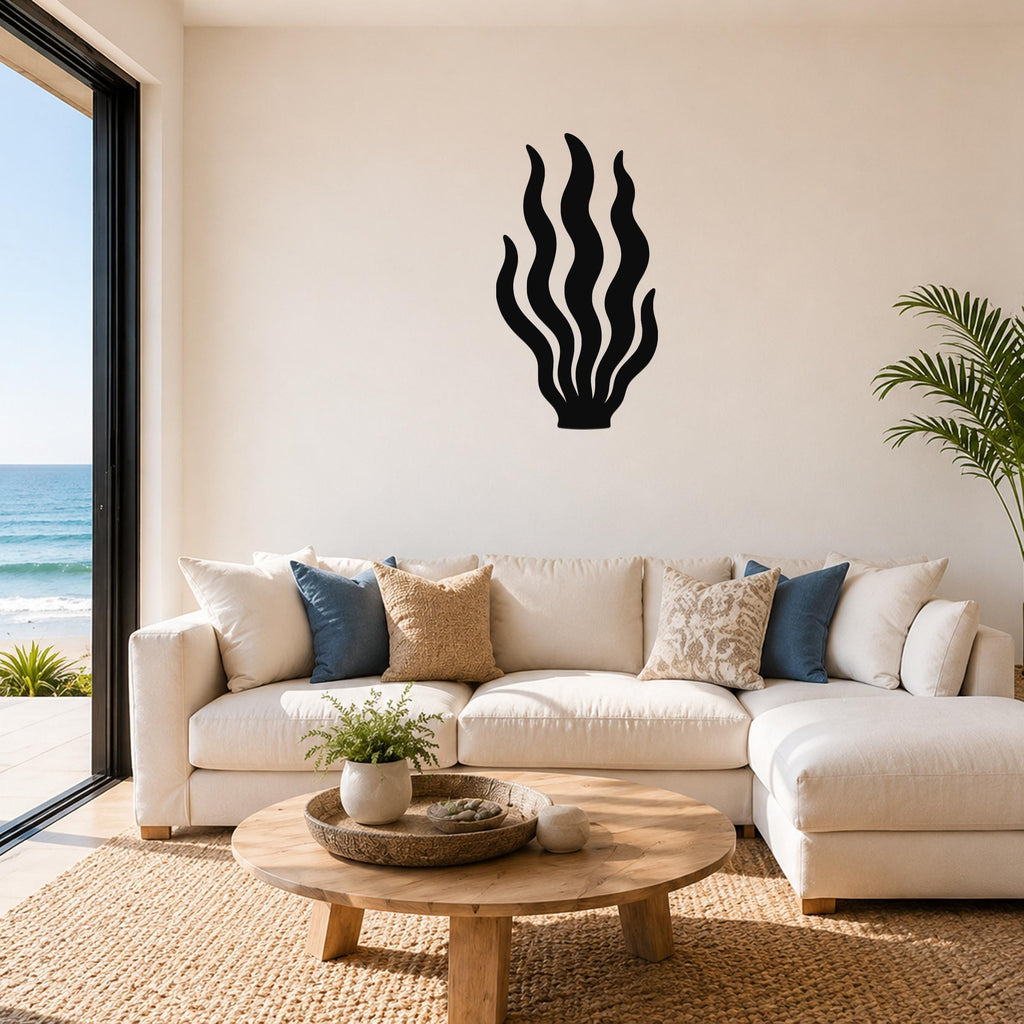 Black metal kelp wall art with flowing wavy cutouts, mounted above a white sectional sofa in a bright living room with ocean views.