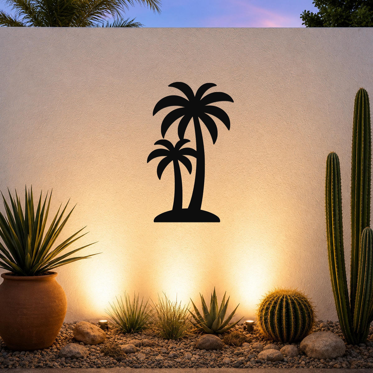 Black metal wall art featuring a silhouette of two palm trees, mounted on an outdoor wall above a desert garden with cacti and warm uplighting.