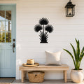 Black metal fan palm tree wall art with three circular fronds and leafy base, mounted on a white shiplap wall above a wooden bench in a porch entryway.