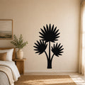 Black metal wall art silhouette of a fan palm tree with three fronds, mounted on a beige bedroom wall above a bed.