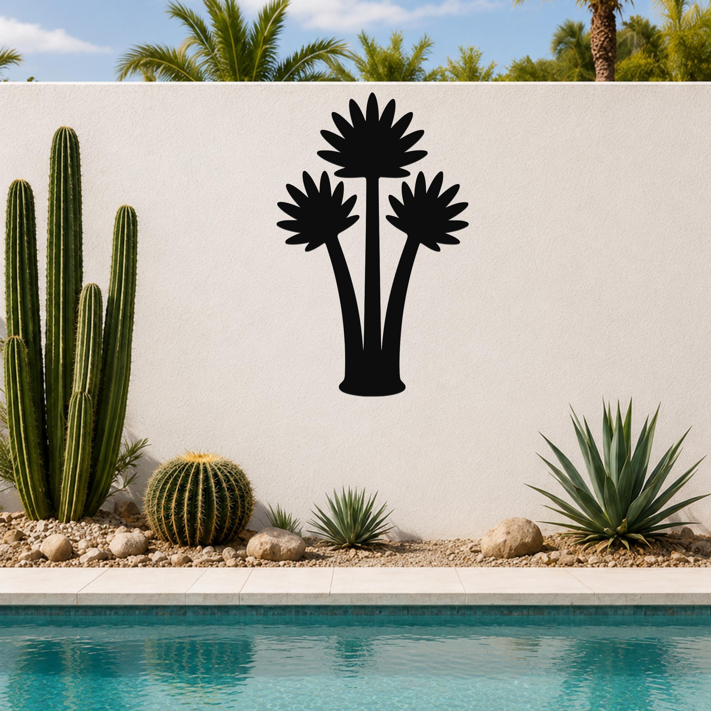 Black metal wall art featuring a fan palm tree silhouette with three fronds, mounted on a white outdoor wall above a pool and desert plants.