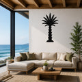 Black metal palm tree wall art silhouette mounted on a white wall above a beige sectional sofa in a coastal living room with ocean views.