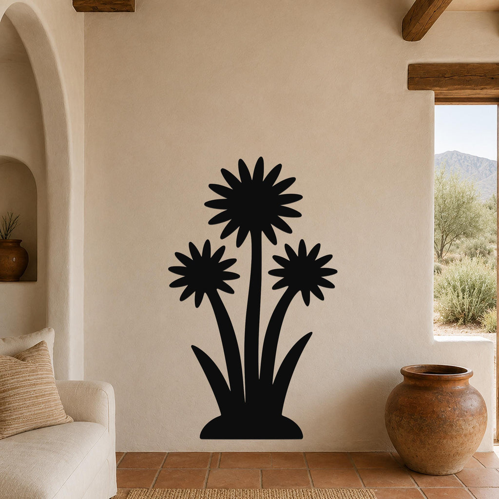 Black metal wall art featuring a silhouette of three wildflowers with pointed petals and long stems, mounted on a beige stucco wall in a living room with terracotta flooring and wooden beams.