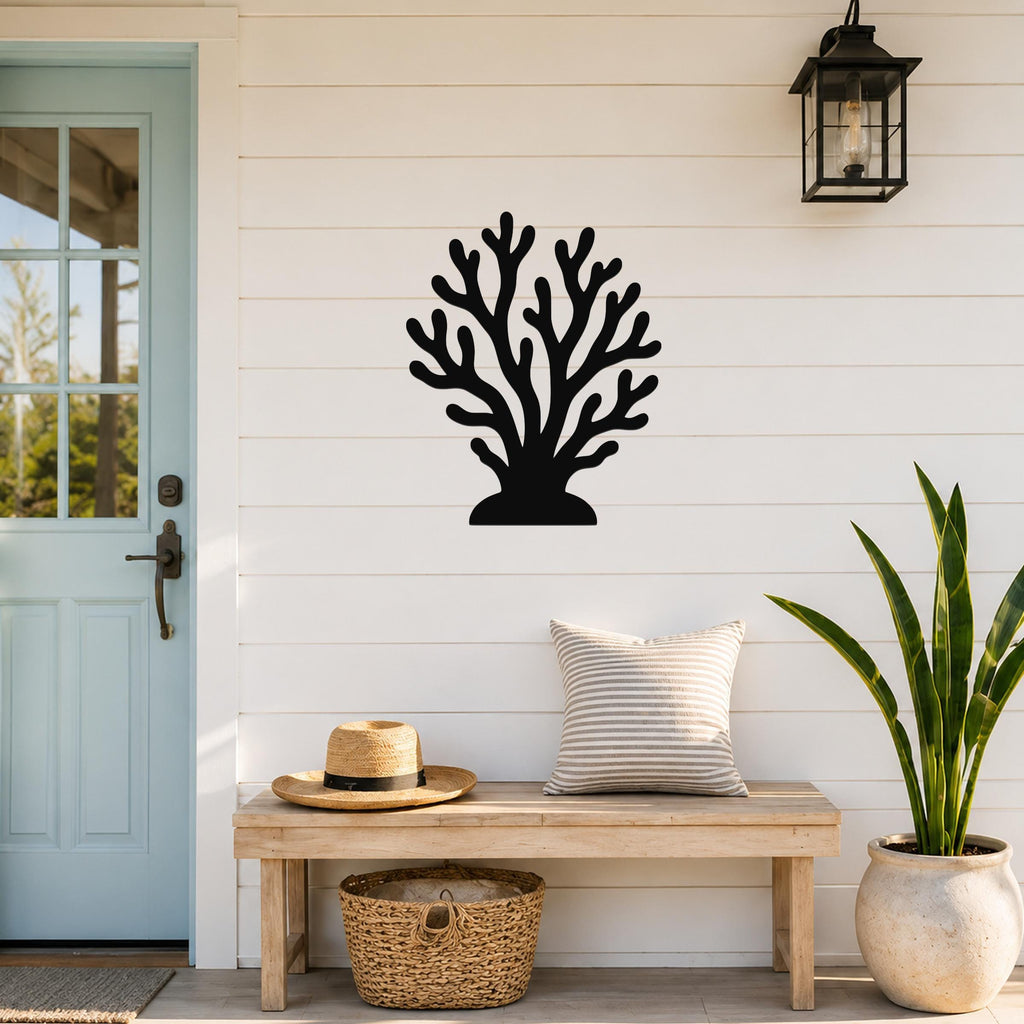 Black metal coral wall art with branching cutouts, mounted on a white shiplap wall above a wooden bench in a coastal entryway.