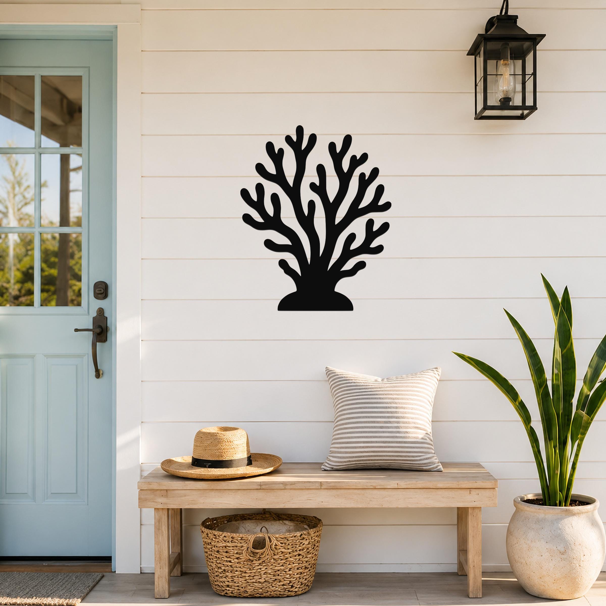 Black metal coral wall art with branching cutouts, mounted on a white shiplap wall above a wooden bench in a coastal entryway.