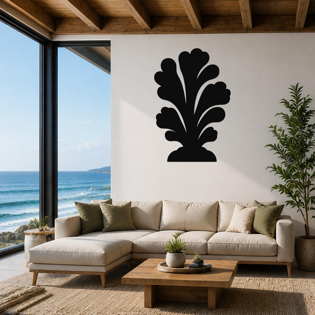 Black metal coral wall art with layered leaf-like cutouts, mounted on a white wall above a beige sectional sofa in a living room with ocean views.