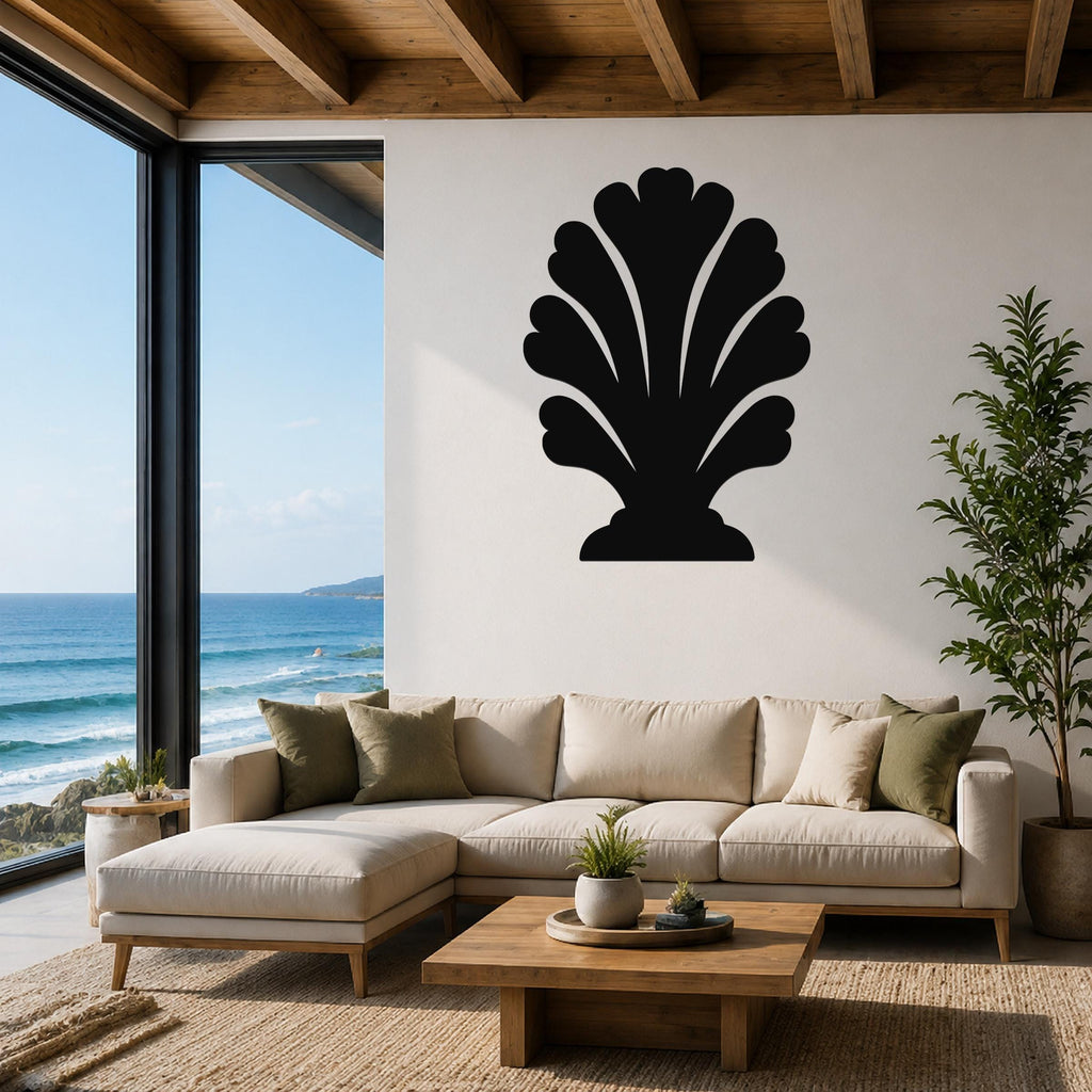 Black metal wall art in a shell silhouette design, mounted on a white wall above a beige sectional sofa in a coastal living room with ocean views.