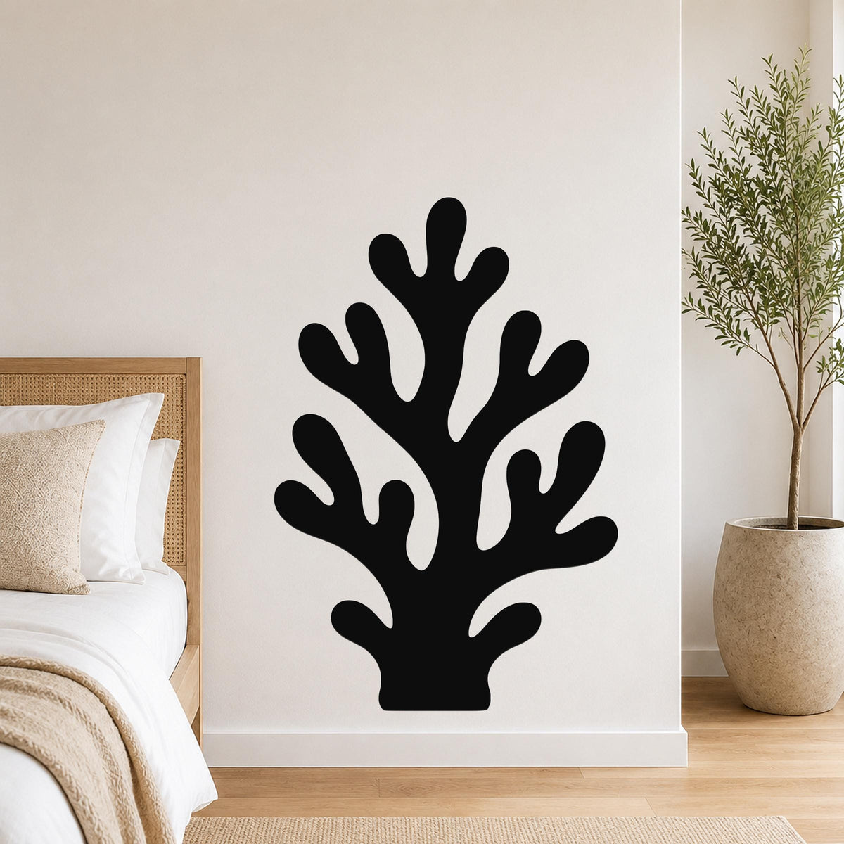 Black metal coral wall art with branching cutouts, mounted on a white bedroom wall above a bed.