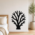 Black metal wall art in a branching coral silhouette, mounted on a white bedroom wall above a bed with a woven headboard.