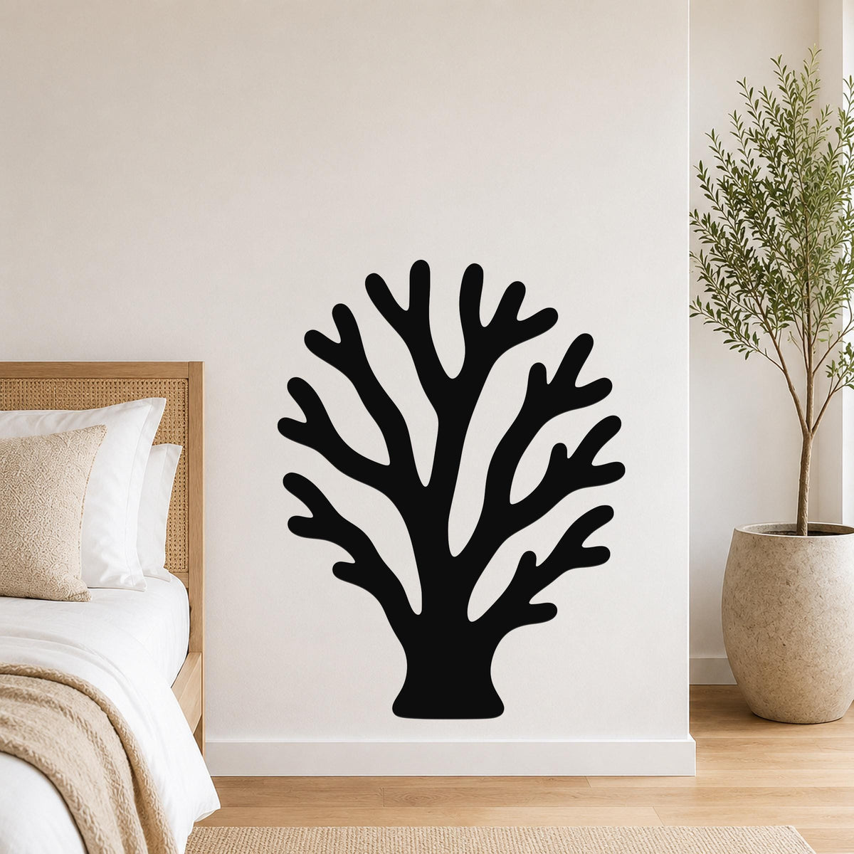 Black metal wall art in a branching coral silhouette, mounted on a white bedroom wall above a bed with a woven headboard.