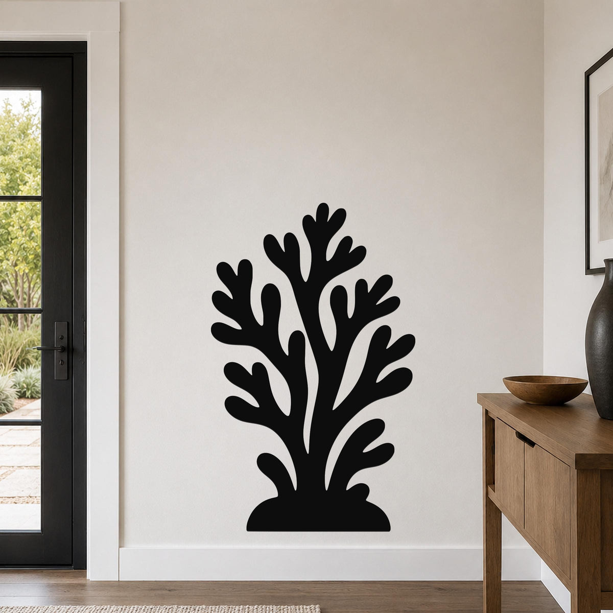 Black metal coral wall art with branching cutouts, mounted on a white wall in a living room near a door and console table.