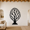 Black metal wall art in the shape of a fan coral with intricate cutout branches, mounted on a living room wall above a sofa.