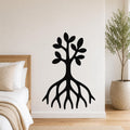 Black metal wall art in a tree silhouette with visible roots and leafy branches, mounted on a white bedroom wall above a bed.
