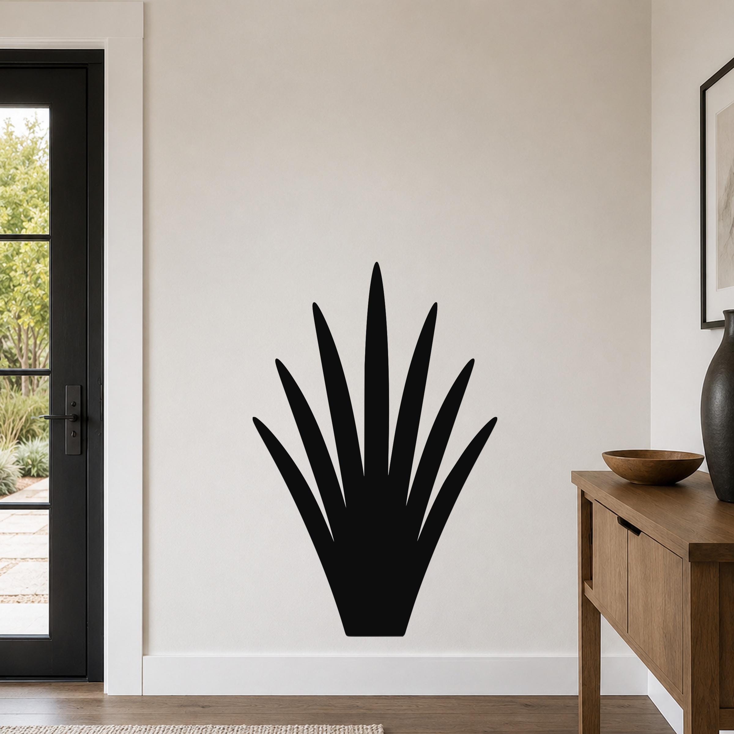 Black metal yucca wall art with spiky leaf cutouts, mounted on a white wall above a wooden console table in a living room.