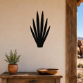 Black metal yucca wall art silhouette mounted on a beige stucco wall above a wooden table in a desert-style patio setting.