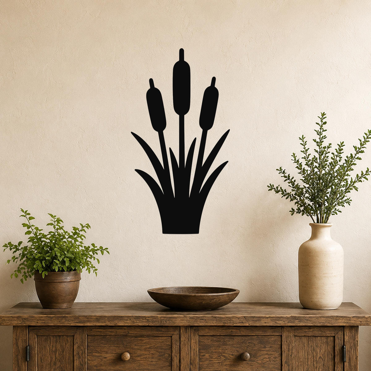 Black metal cattail wall art silhouette with three seed heads and leaf cutouts, mounted on a beige wall above a wooden console table in a living room.