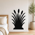 Black metal wall art in a cattail silhouette design, mounted on a bedroom wall above a bed with a woven headboard.
