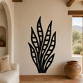 Black metal wall art in a snake plant silhouette with internal cutout details, mounted on a beige living room wall above a sofa.
