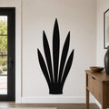 Black metal wall art in the silhouette of a snake plant, mounted on a light-colored wall in a modern entryway.