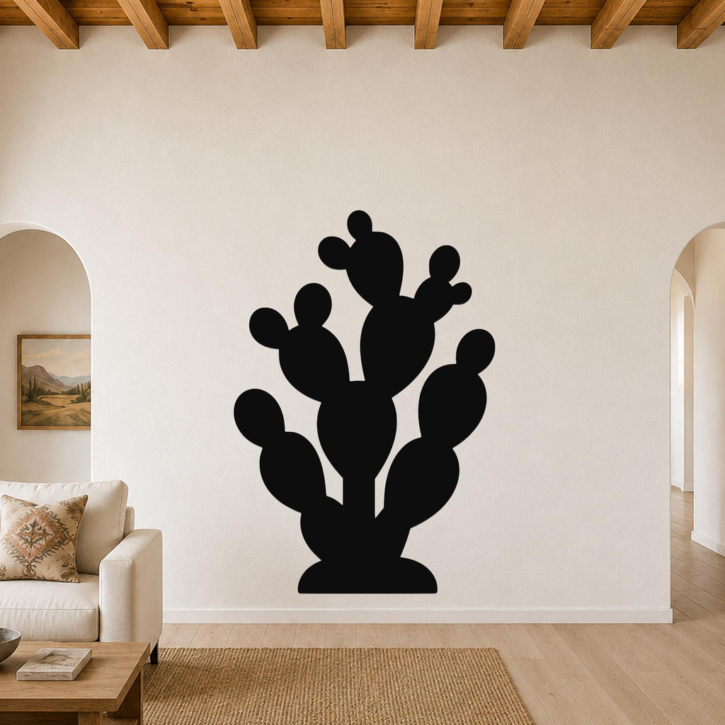Black metal prickly pear cactus wall art with multiple segmented pads and cutout details, mounted on a white living room wall above a beige sofa.